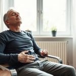 Adulte assis près d’une fenêtre, yeux fermés, main sur l’abdomen